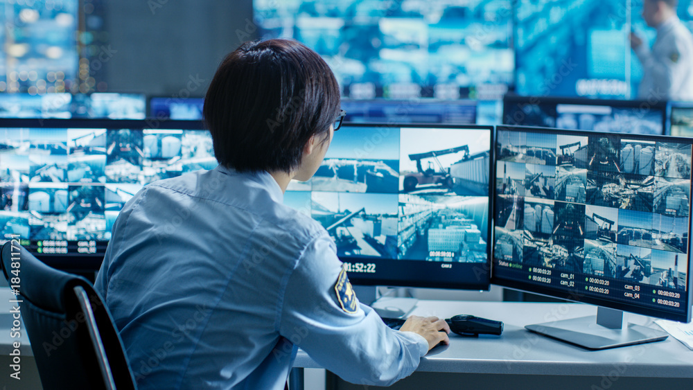 Poster in the security control room officer monitors multiple screens for suspicious activities. he's surro
