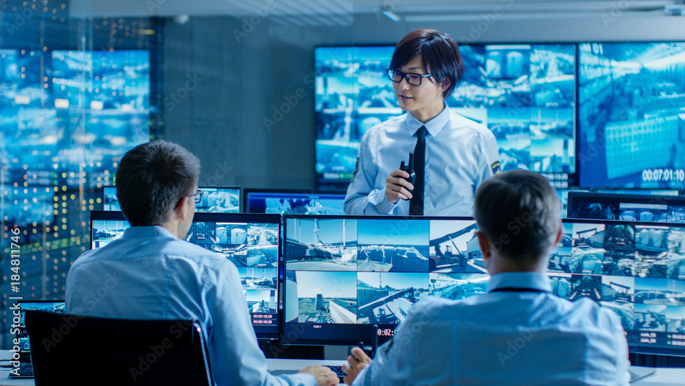 Poster in the security control room chief surveillance officer briefs two of his subordinates. multiple scr