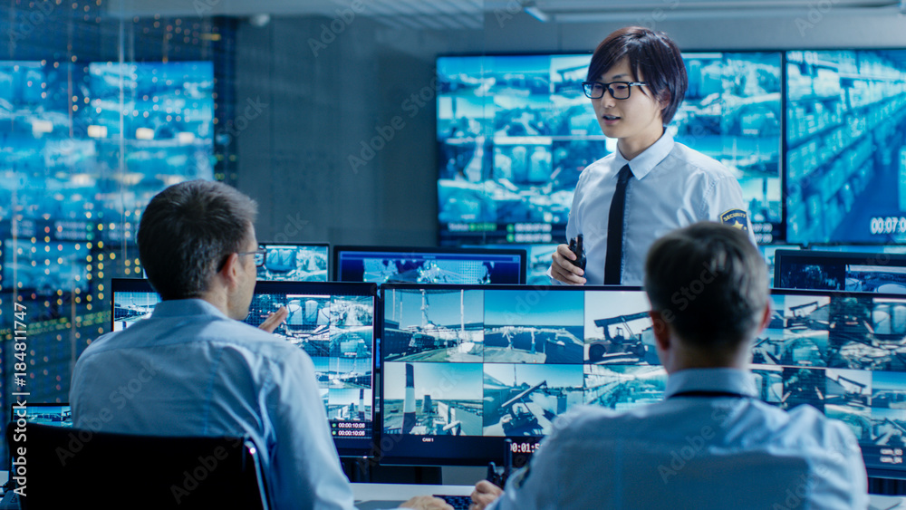 Poster in the security control room chief surveillance officer briefs two of his subordinates. multiple scr