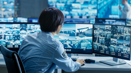In the Security Control Room Officer Monitors Multiple Screens for Suspicious Activities. He's...