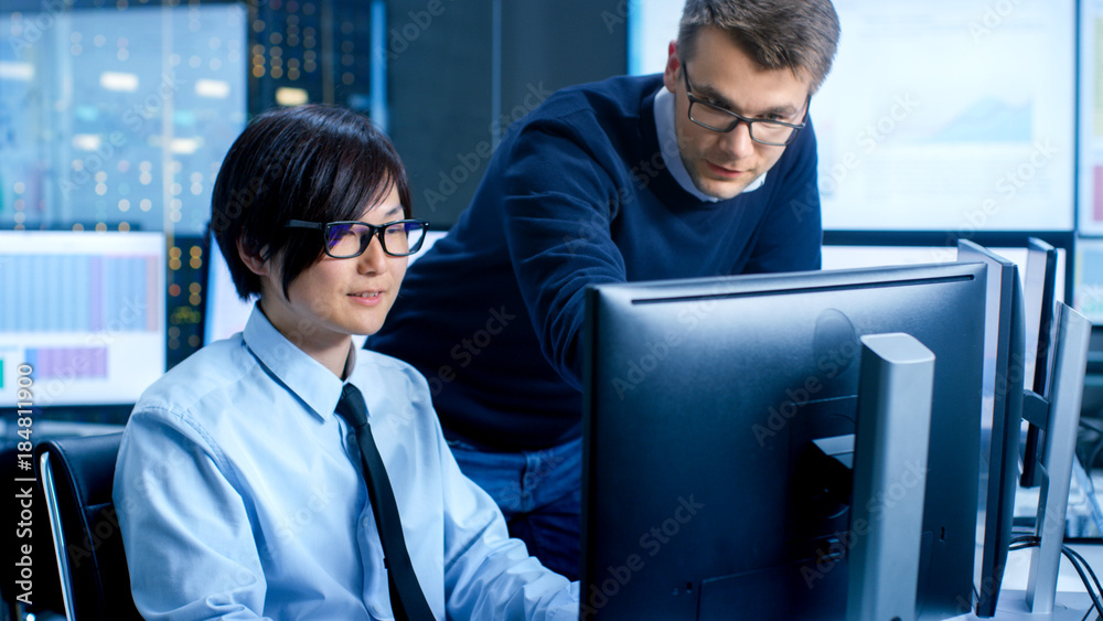 Poster In the Data Mining Center Chief Statistician Consults His Young Assistant sits at His Workstation Surrounded with Monitors Displaying Data and Graphs.