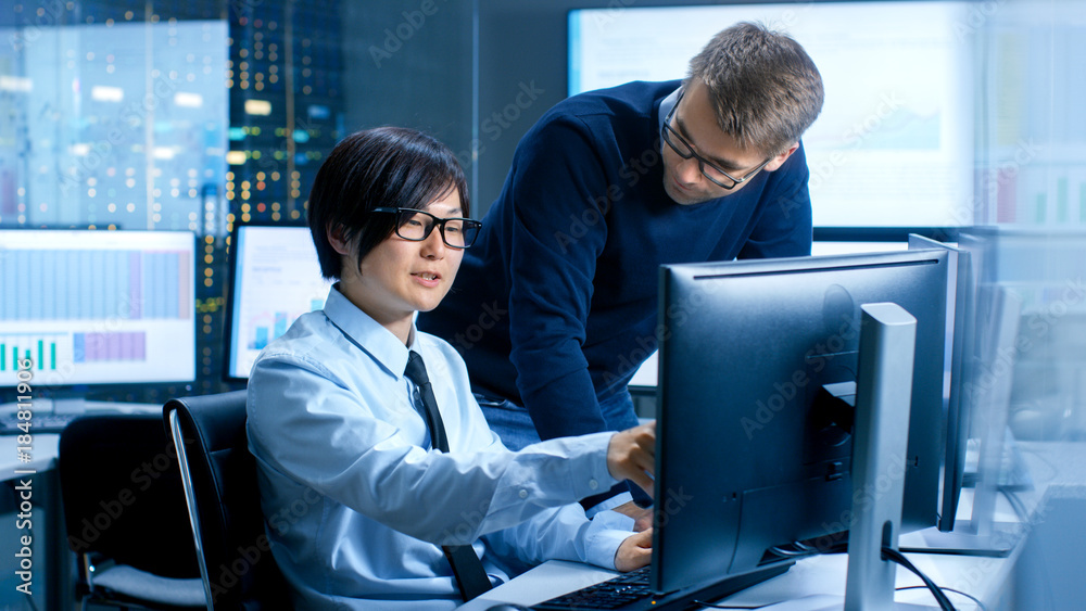 Poster In the Data Mining Center Chief Statistician Consults His Young Assistant sits at His Workstation Surrounded with Monitors Displaying Data and Graphs.