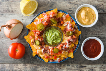 Mexican nachos with beef, guacamole, cheese sauce, peppers, tomato and onion in plate on wooden table. Top view
