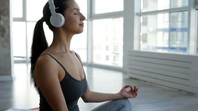 Satisfaction. Close up of young positive woman sitting on the floor with her eyes closed while listening to the music and doing yoga