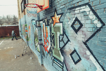 man painting colorful graffiti on wall with basketball hoop