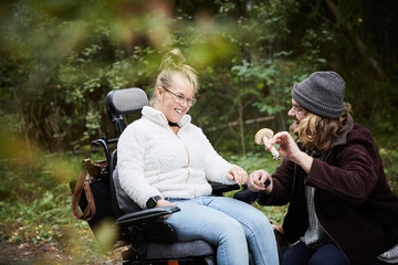 Male caretaker showing mushroom to disabled woman in wheelchair at forest