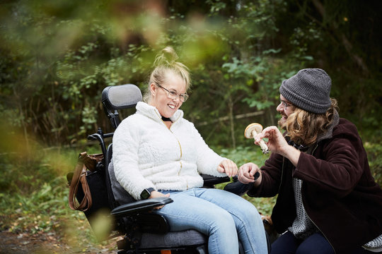 Male caretaker showing mushroom to disabled woman in wheelchair at forest