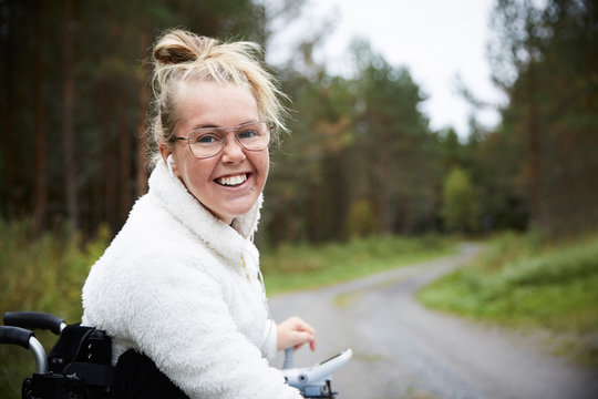 Portrait of smiling young disabled woman sitting in wheelchair on road