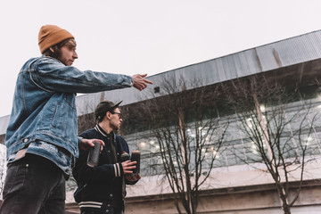 male street artists holding cans with spray paint and pointing on building