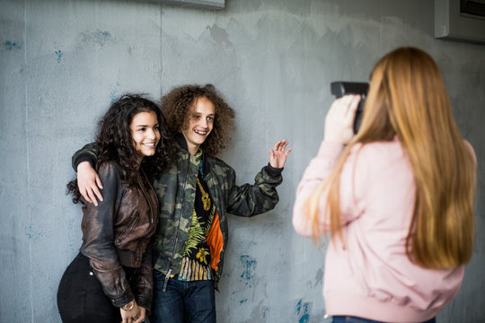 Rear view of girl photographing smiling teenage friends standing against wall at parking garage