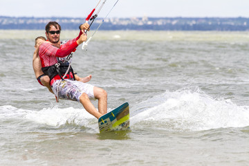 Fototapeta premium Dad and son are kitesurfing on the sea. The son clings to Papa's back