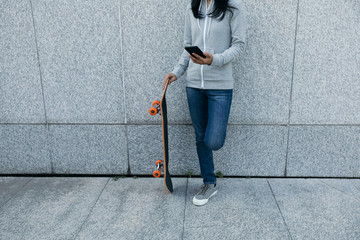 female skateboarder using smartphone leaning on wall in city