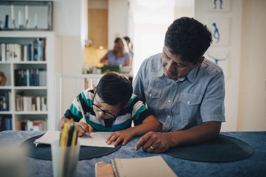 Father assisting son in homework while sitting at table