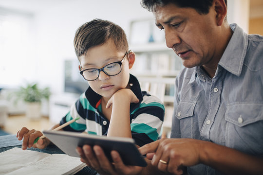 Father showing digital tablet to son while studying at table