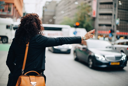 Rear view of mid adult businesswoman hailing taxi on street in city