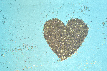 Abstract heart of golden glitter sparkles on blue background. Photographic filters were used, nostalgic colors 