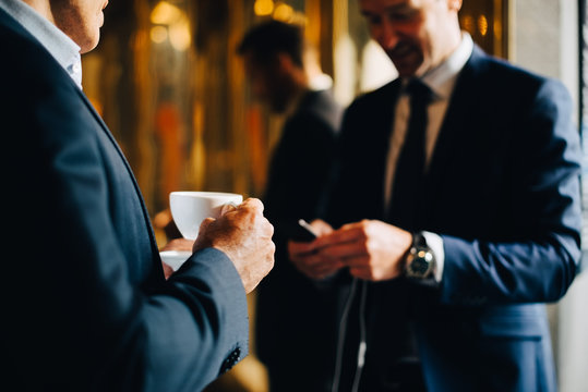 Midsection of businessman drinking coffee while standing by colleague using mobile phone in cafe