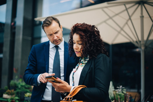 Businessman and businesswoman sharing mobile phone against parasol in city