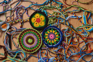 Different kind of knitted colorful bracelets and earrings are chaotically lying on the table. In the lower left side there are three big knitted drink coasters.