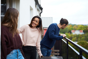 Smiling young friends standing in balcony at rental apartment