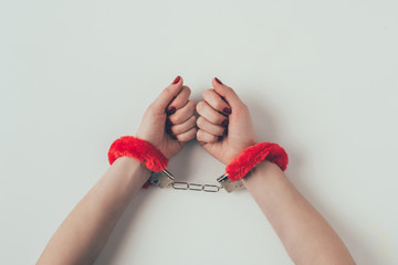 cropped image of woman hands in red fluffy handcuffs on white