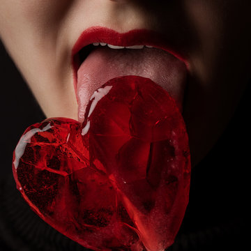 cropped image of woman licking heart shaped lollipop isolated on black