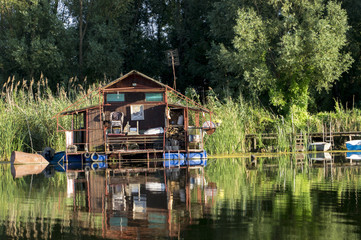 Floating house in the swamp. Pontons provide floating on the water. Old raft with neatly arranged details. The environment of lush vegetation of trees and reeds.