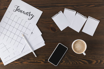 flat lay with empty notebook, calendar, pencil and smartphone on wooden surface