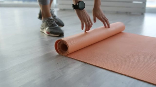 Preparation. Close up of energetic woman slowly unrolling training mat on the floor