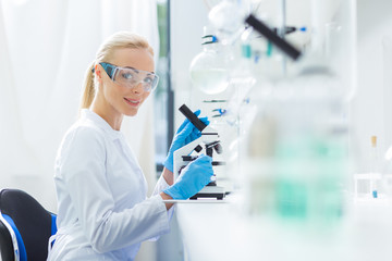 Delighted female biologist sitting in front of the microscope