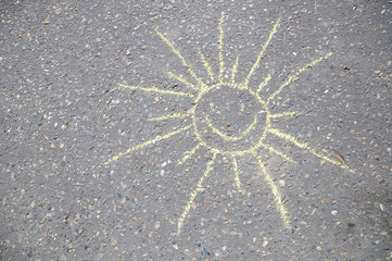 Smiling sun painted with face by chalks on asphalt,.smiley sign sketched outdoor by children while walking in the park