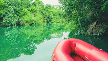 Red boat on the river. River with green water, beautiful nature landscape. Red inflatable boat for...