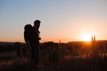 Traveler with backpack standing on a rock and enjoying sunset
