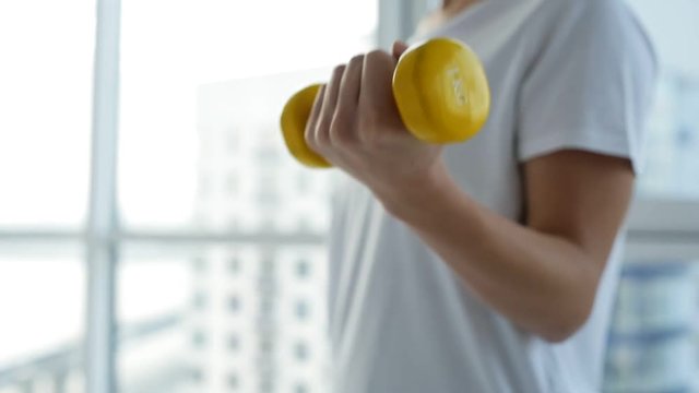 Strong and healthy. Close up of young sportive woman standing in front of you while training with light weights