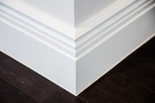 Ornamental moulding in the corner of a white room with dark wood floor interior concept
