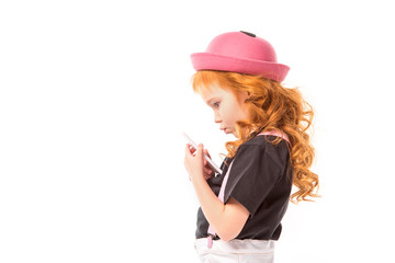 side view of thoughtful red hair kid looking at smartphone isolated on white