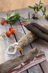 several variety of traditional Corsican charcuterie with an olive branch and black olives on wooden background and arbitus bayberry