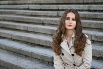 Young beautiful woman wearing beige jacket sitting on concrete stairway