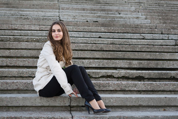 Young beautiful woman wearing beige jacket sitting on concrete stairs