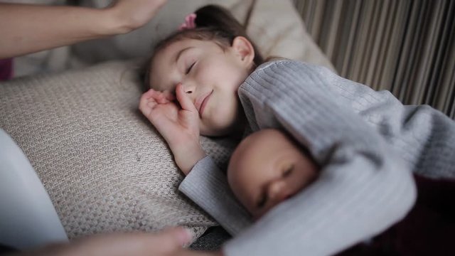 beautiful little girl on a sofa falls asleep and hugging a doll. Mom strokes a sleepy daughter