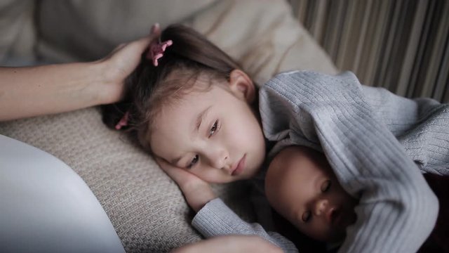 beautiful little girl on a sofa falls asleep and hugging a doll. Mom strokes a sleepy daughter