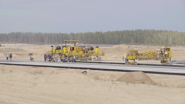 Construction, concreting of airport runways roads. Men, workers working with asphalt paver, resting. Roadroller, construction machinery works on new runway construction of national airport Minsk, MSQ