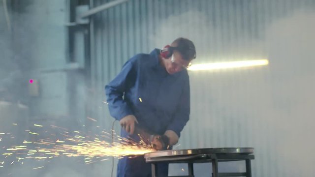 Worker in protective headphone and eyewear grinding metal for final processing
