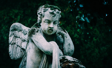 Mystic old statue of the praying angel. Sad mossy sculpture of the angel pray for the god.