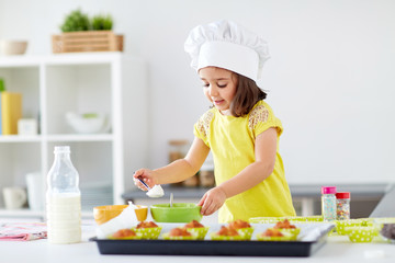 little girl in chefs toque baking muffins at home - obrazy, fototapety, plakaty