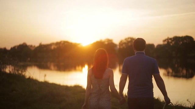 A loving couple on a date at sunset by the river. the guy and the girl are walking along the coast in the rays of sunset