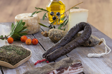 several variety of traditional Corsican charcuterie with an olive branch and black olives on wooden...