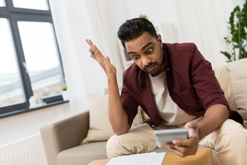 confused man with papers and calculator at home