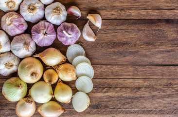 Fototapeta na wymiar Onions and cut onions, purple whole garlic and garlic cloves on top of a light wooden background, with lots of texture and copy space