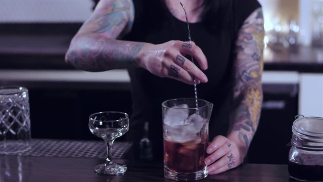 Tattooed bartender lady stirring an alcoholic mixed drink in a thoroughly manner at a bar